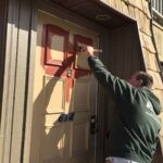 Exterior metal door and an apartment complex being painted red using a brush