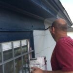 Exterior trim on the second floor of a house being painted blue by brush