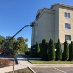 Two men and a boom lift painting tan wall on the side of a four-story hotel