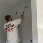 Men wearing DJ's Painting shirt painting interior wall with a roller
