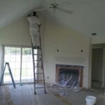 Man standing on the ladder painting wall in a Family room with vaulted ceilings