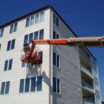 Man in a boom lift applying caulk to waterproof a window on a multi family condominium building
