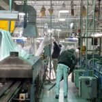 Men cleaning under equipment and covering equipment with plastic and a food production facility