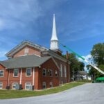 220 foot boom lift extended halfway up a steeple while painters apply white paint to the steeple