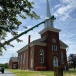 Two men on a 220 foot boom lift painting a white steeple on a historic church building