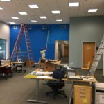 Interior commercial office space being painted by two men using rollers and long poles