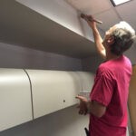 Man painting gray wall in an office along the edge of drop ceiling with a brush