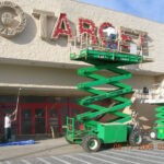 Two men painting the front entrance of a target retail store using a roller and brush