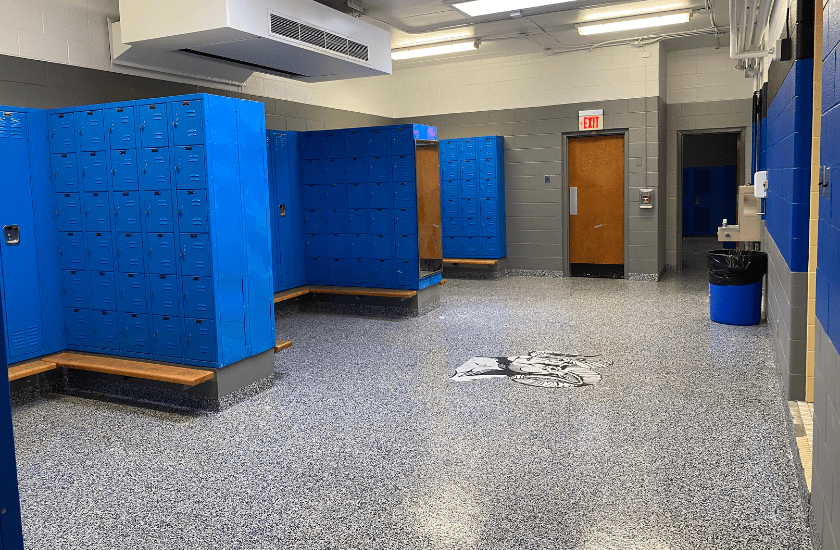 Freshly painted gray walls in a locker room with newly applied black and gray flake floor and a large high school logo in the center of the floor