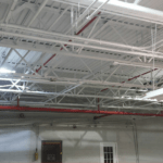 Freshly painted white steel deck warehouse ceiling with red sprinkler pipes