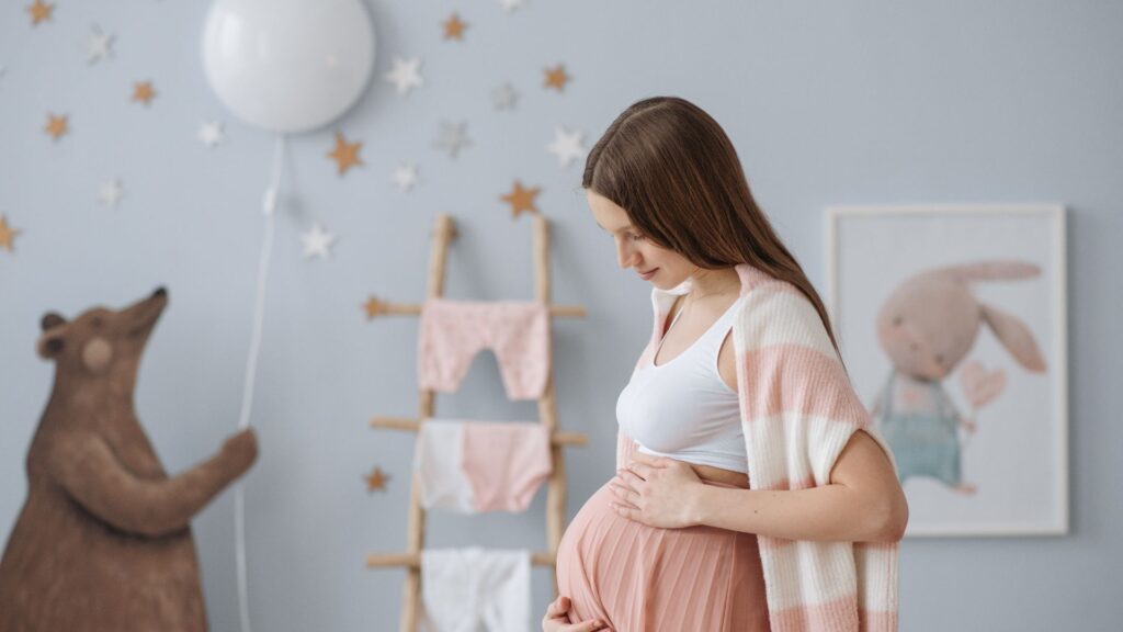 Pregnant woman holding her belly and standing in her baby's nursery.