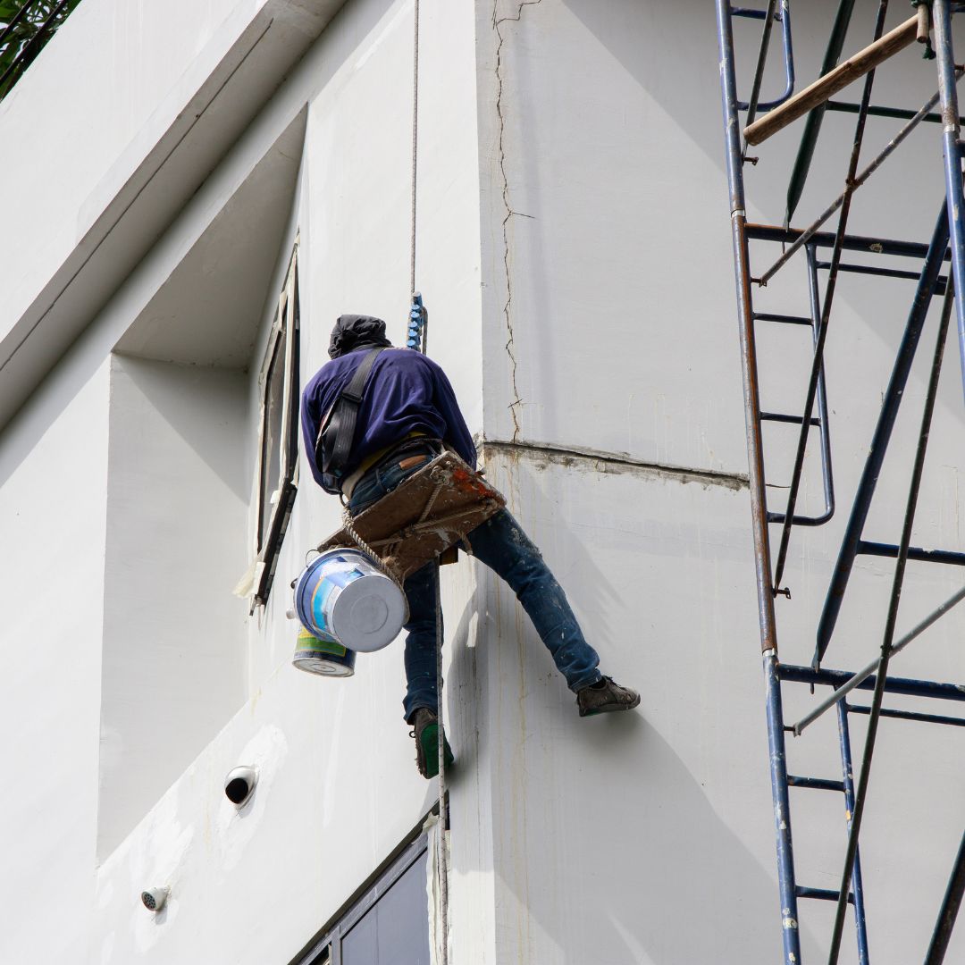 painter hanging on side of the building repairing paint