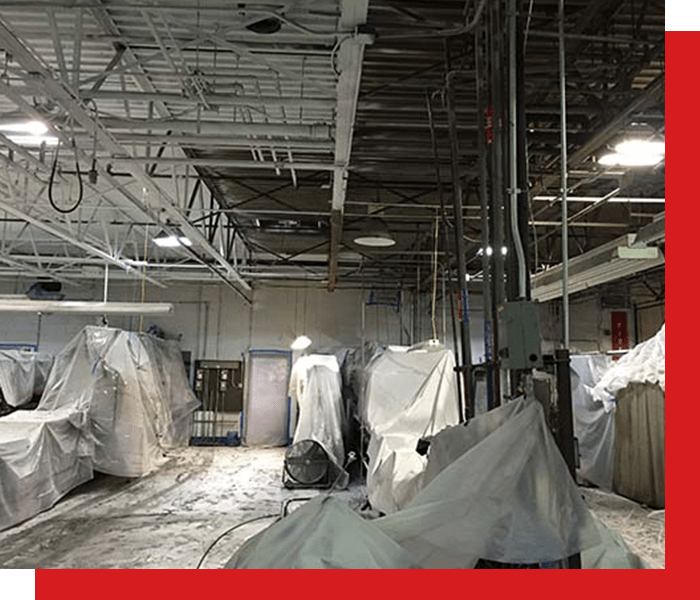 Factory filled with equipment covered by plastic while ceiling is being painted with white dry fog paint