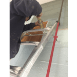 A professional painter fills gaps in a gray cinderblock wall inside of a food processing plant with paintable caulk