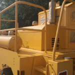 A large piece of heavy construction equipment is freshly painted yellow with 2 component resin paint