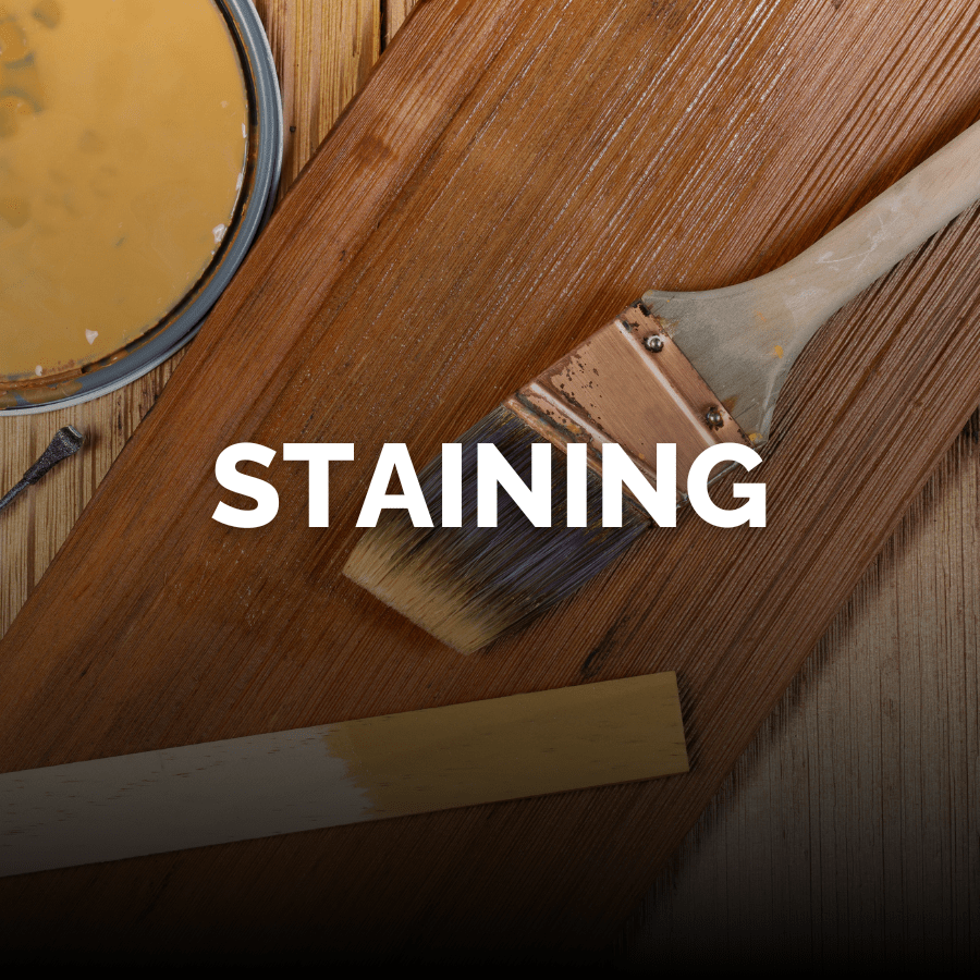 A paint brush, wood stirring stick, and the lid from a can of amber colored wood stain near a piece of brown, stained wood with the word Staining across the middle