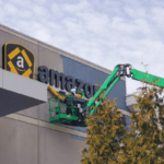 Painters in a articulating boom lift painting gray wall around Amazon sign on an Amazon warehouse