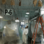 industrial building with floor & equipment covered. ceiling is getting spray painted by a painter  