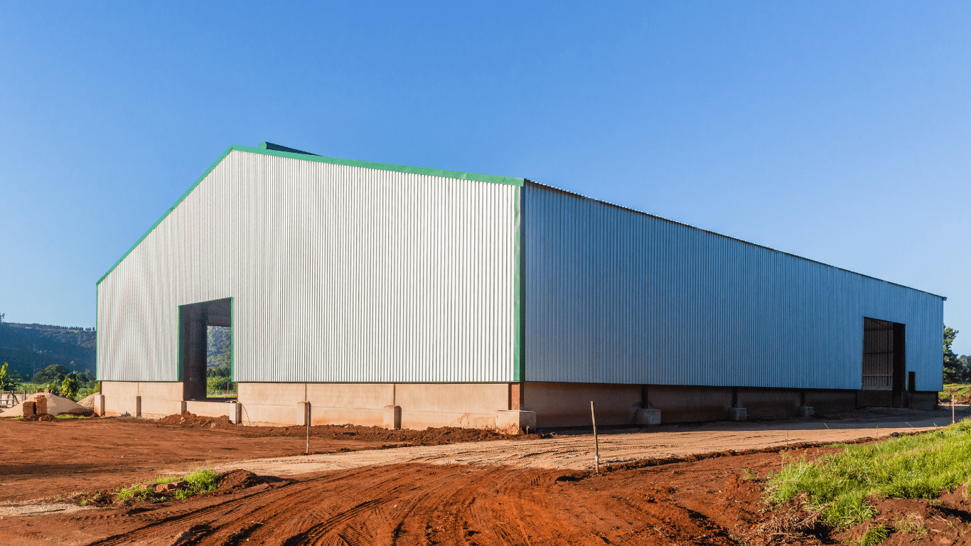 The exterior of a large pole barn or pole building during construction. The walls are gray metal and the metal trim is painted green.