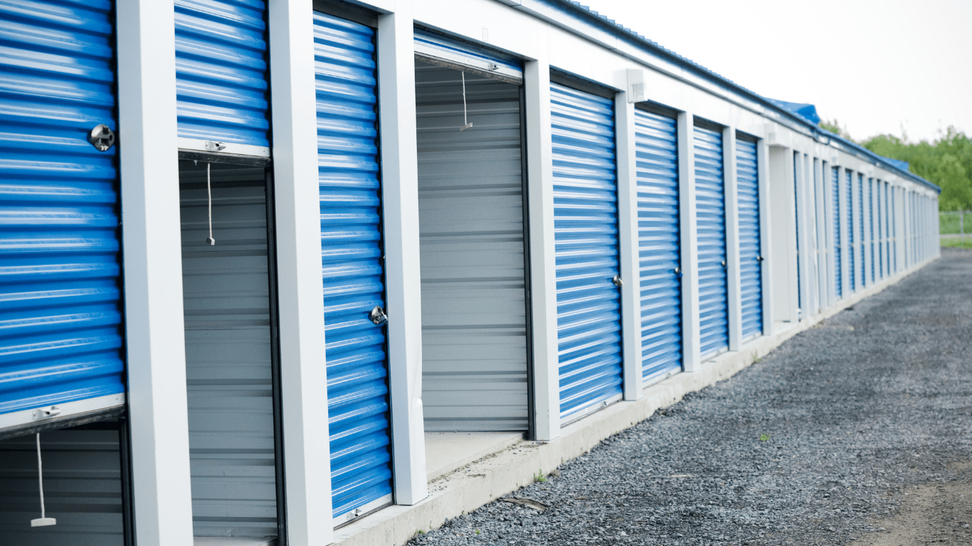 Exterior of a self storage facility with blue metal overhead doors and a blue metal roof. several of the doors are open