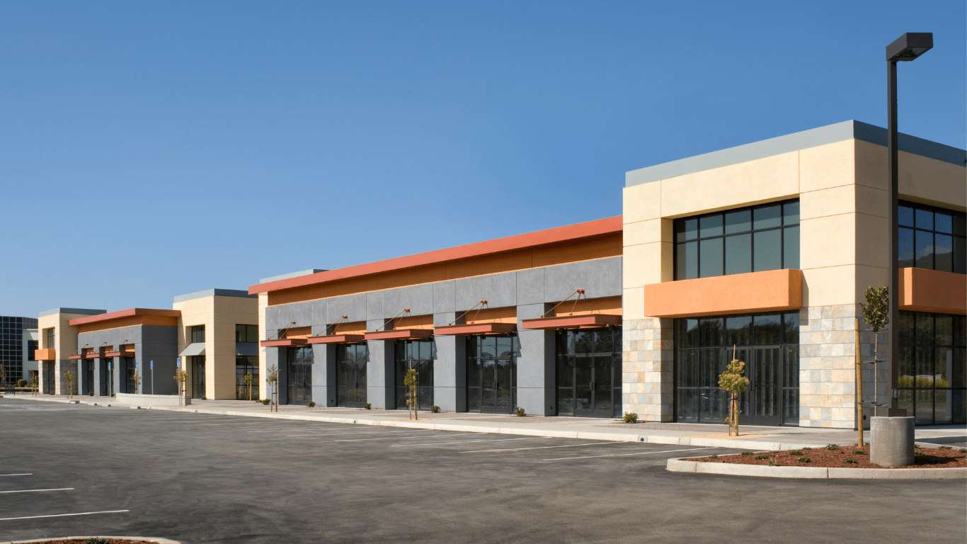 A strip mall or shopping center with beige stucco and orange, red, and gray accents.